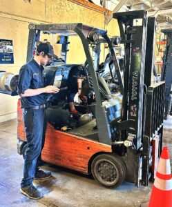 Forklift technician inspecting an aging warehouse forklift to evaluate whether it should be repaired, rehabbed, or replaced