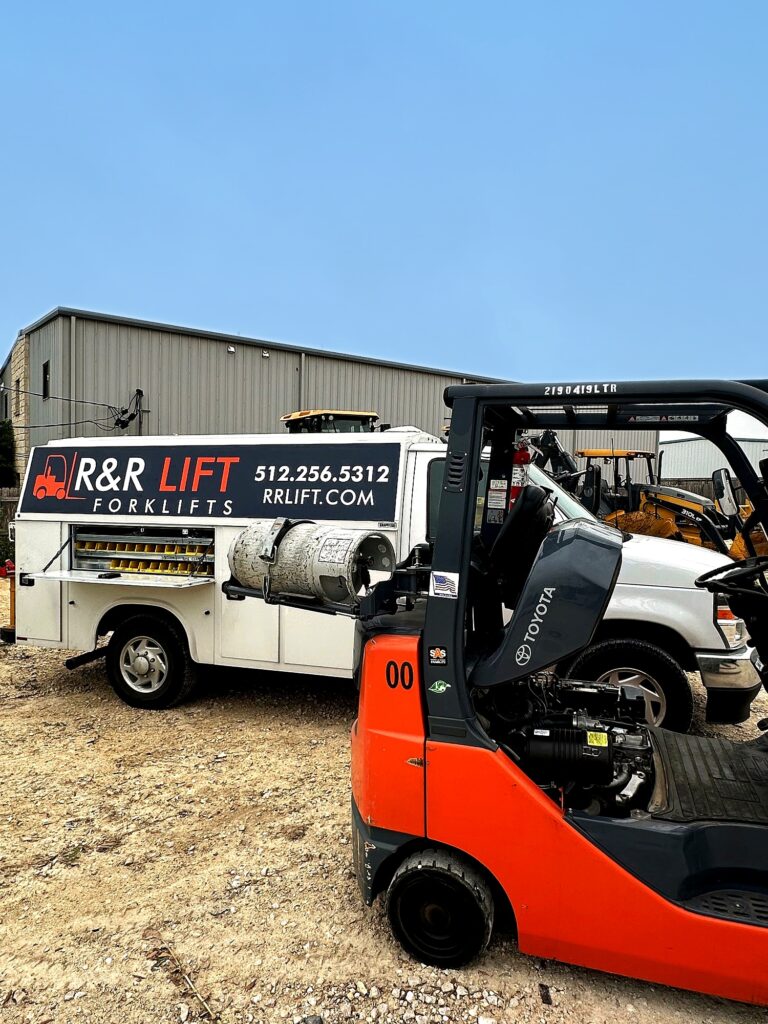Fleet manager reviewing forklift repair costs and lifecycle data while a technician inspects equipment in a warehouse