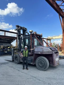 R&R Lift technician beside a large forklift in an outdoor yard