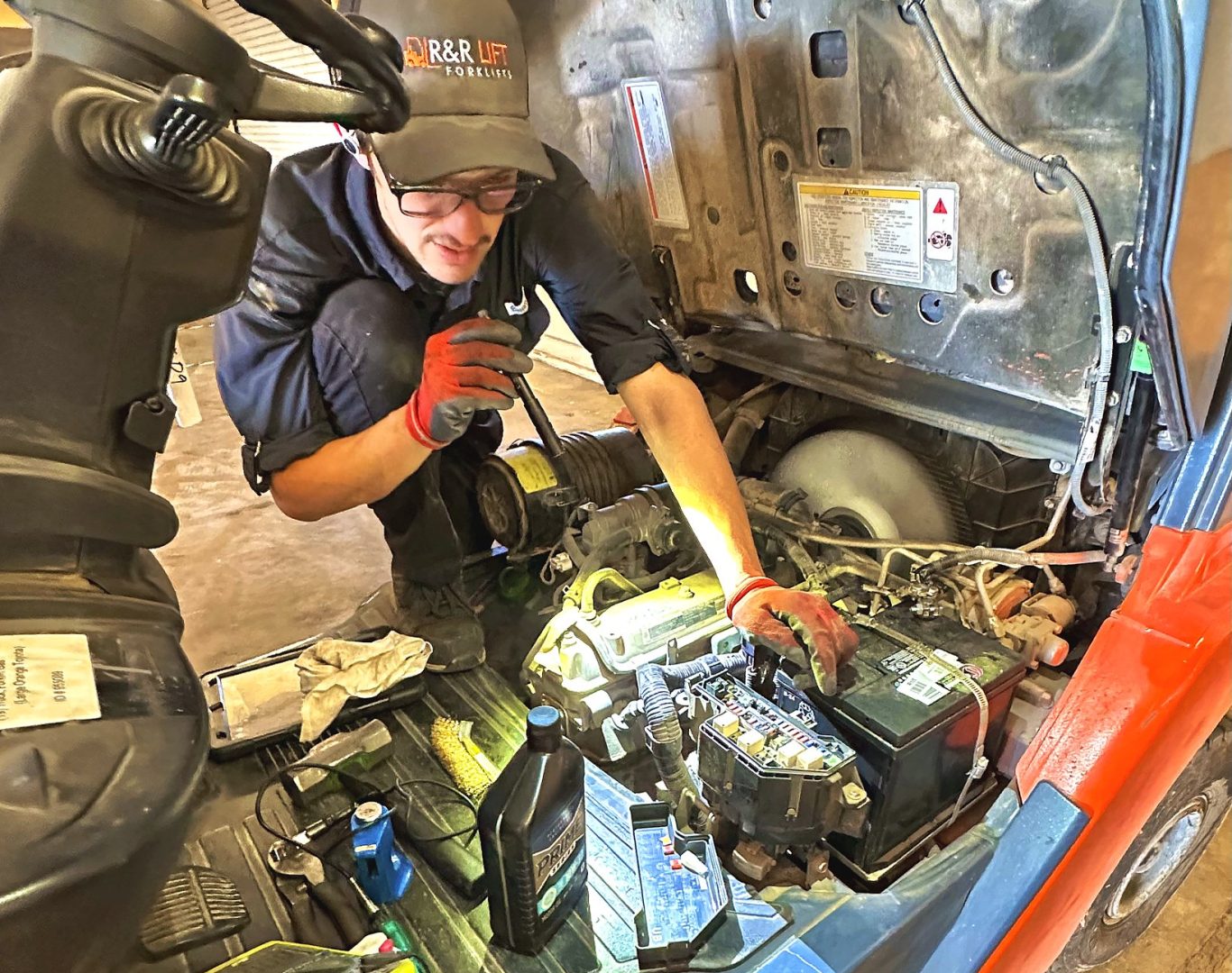 Forklift technician servicing an electric warehouse forklift inside a busy Central Texas distribution center